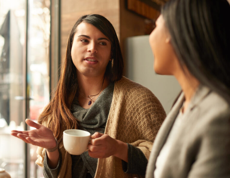 Cropped shot of an affectionate young gender fluid person having a discussion with their friend while having coffee in a cafe