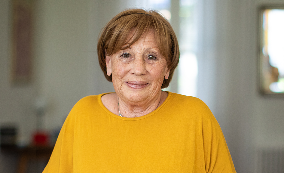 A mature woman smiling directly to camera in a yellow t-shirt
