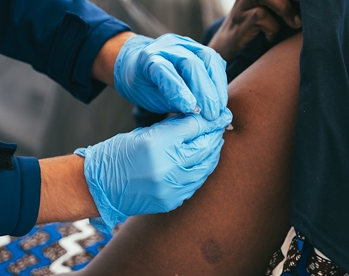 Healthcare worker wearing blue gloves administering a vaccine injection into a person's upper arm.
