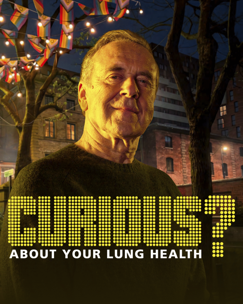 Curious about your lung health? An older White man smiles into the camera. In the background is Canal Street in Manchester, with Pride flag bunting handing in the trees.